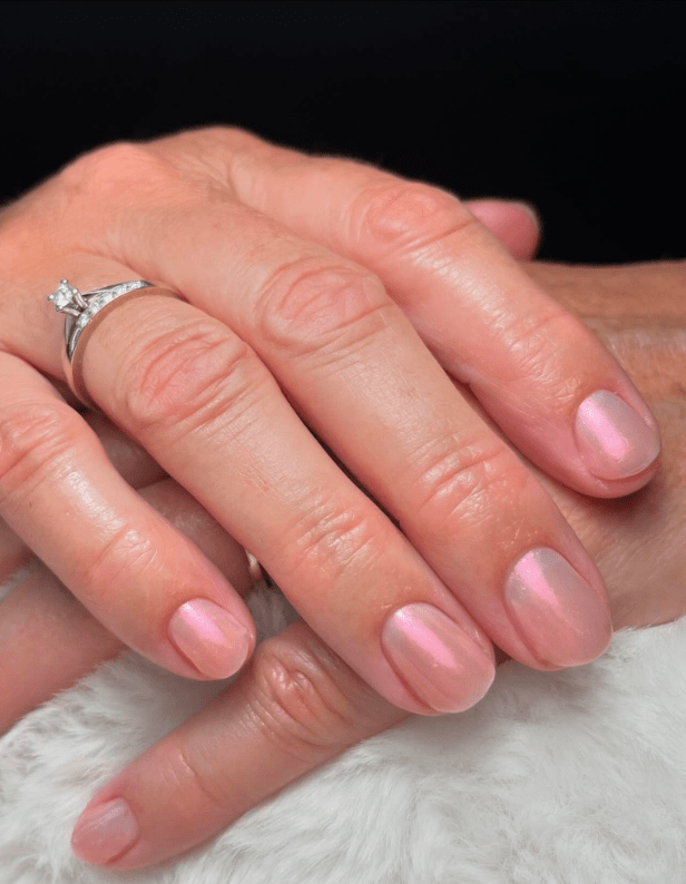 A hand with shiny pink nail polish and a diamond ring on the ring finger, resting on a white, fluffy surface.