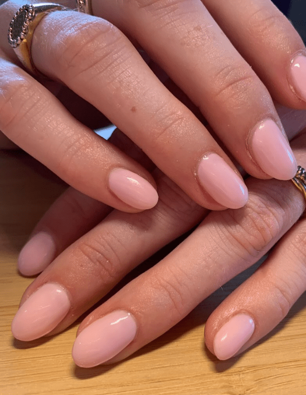 Hands with light pink manicured nails and some rings, on a wooden surface.