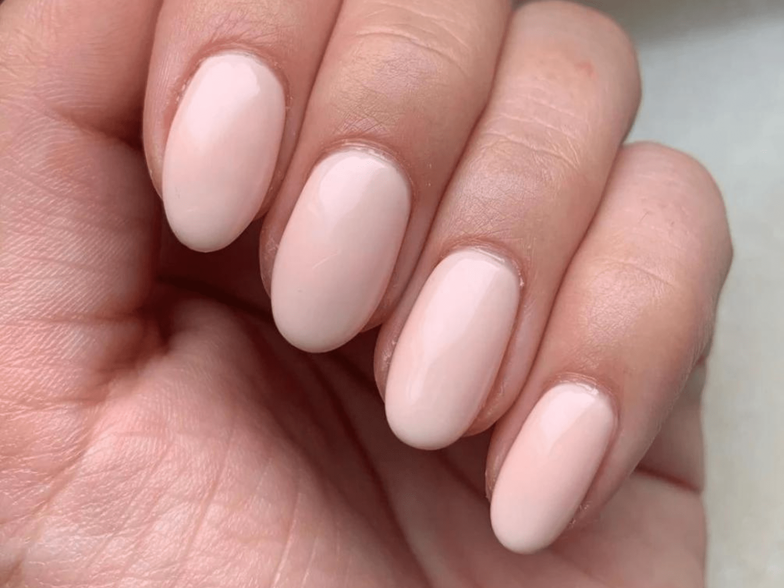 A hand with short-cut, oval nails painted in a light, neutral color.