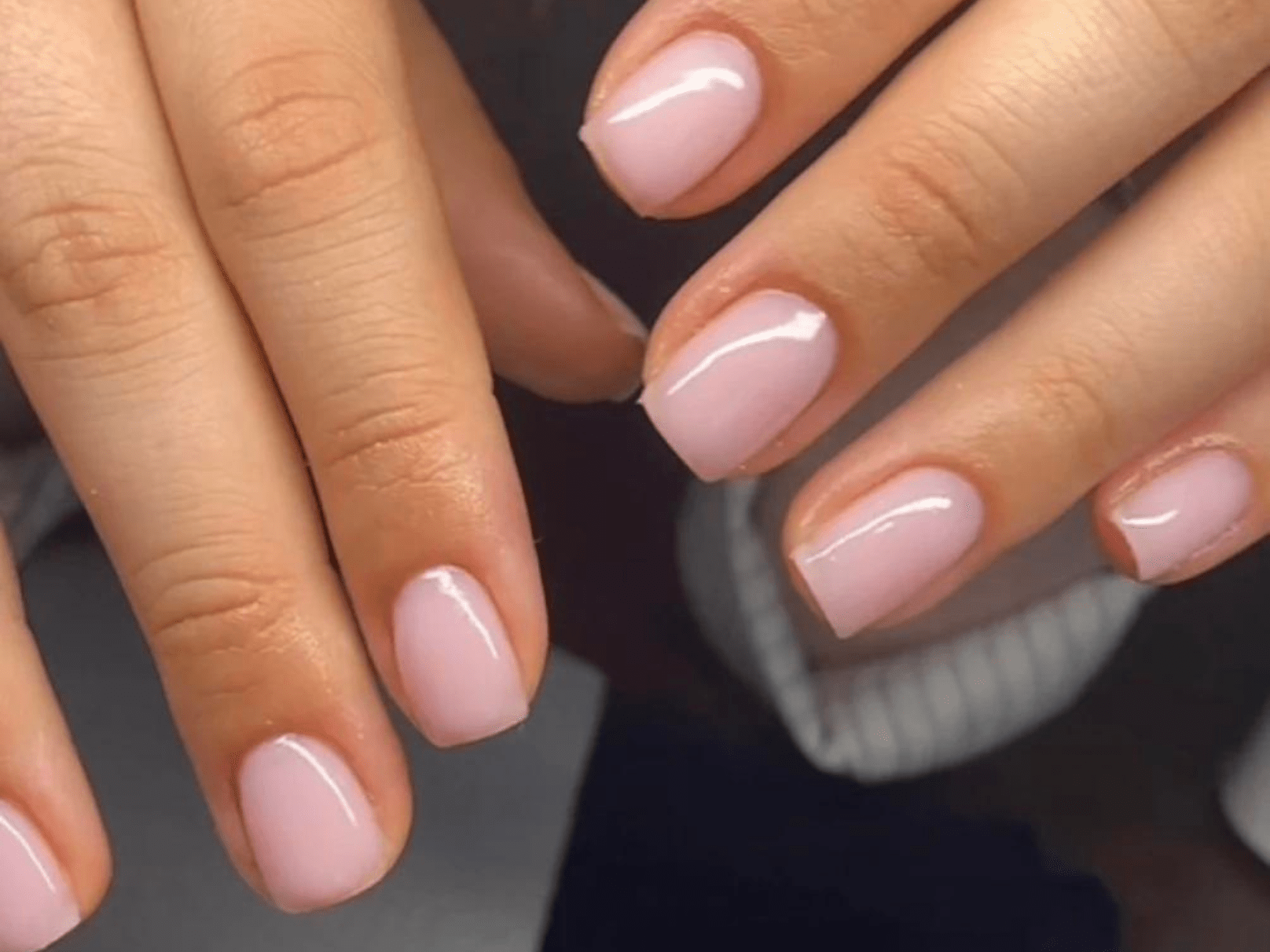 Two hands with short-cut and light pink painted nails.