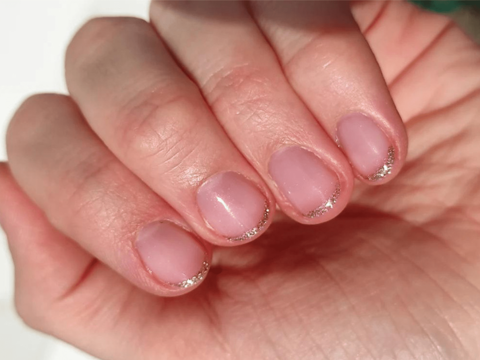 Close-up of a hand with nails painted in a light pink color, with silver glitter on the nail edges.