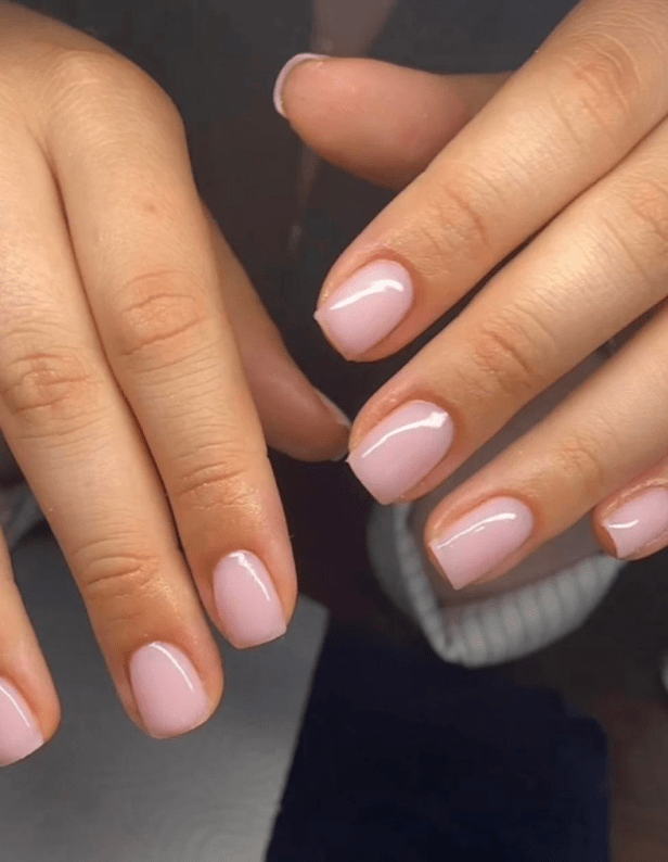Two hands with short nails painted in a light pink color.