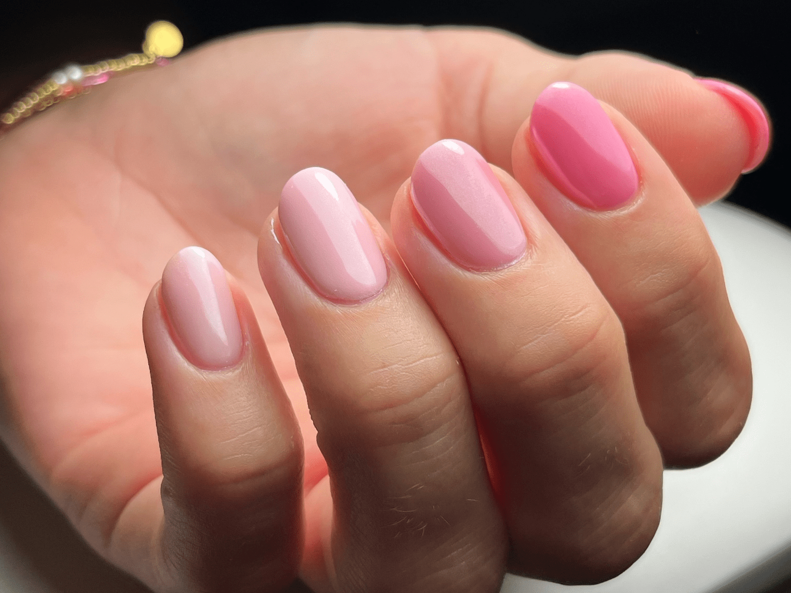 Hand holding shiny, pink gel nail polish in different shades of pink on well-groomed nails.