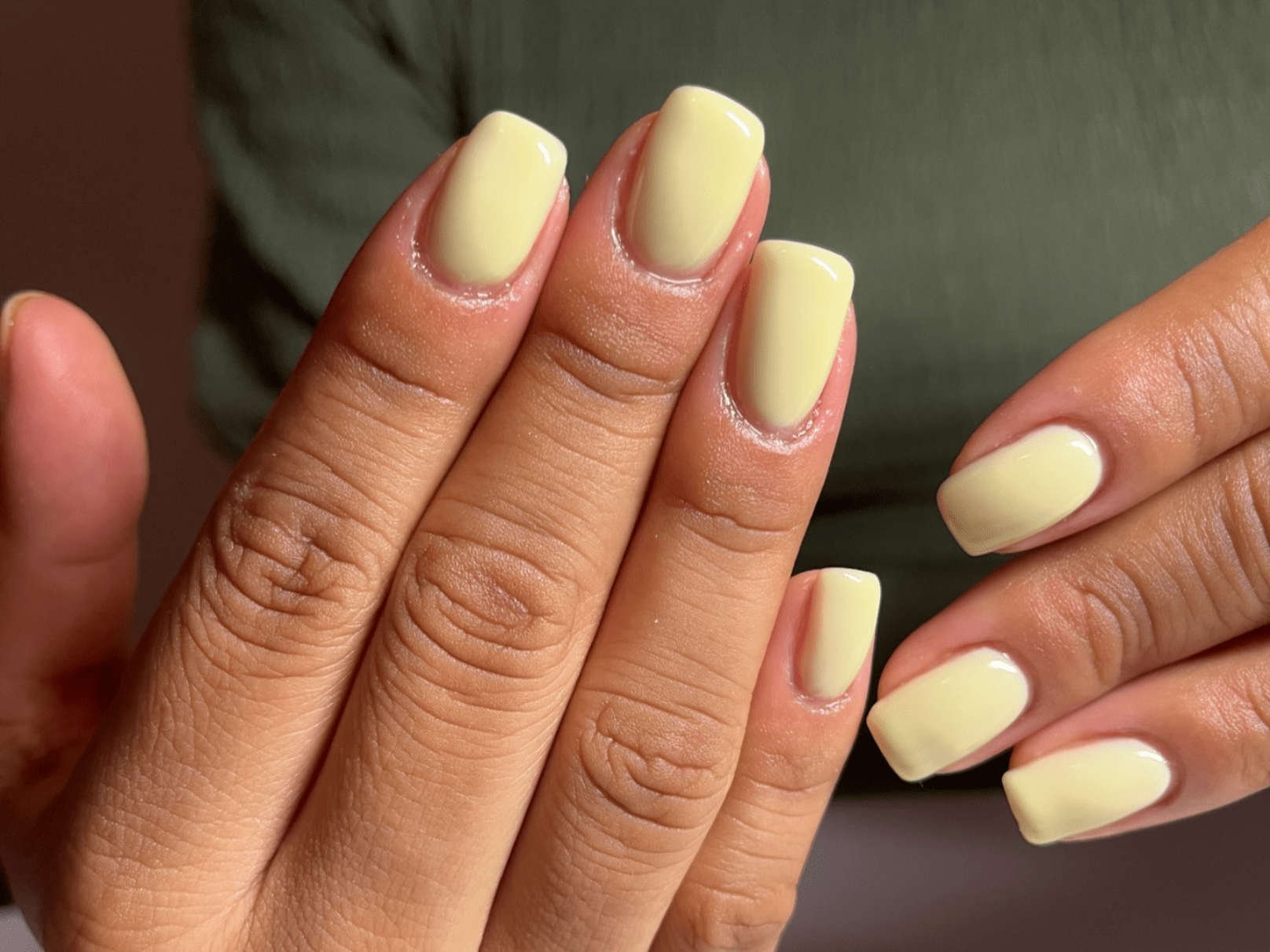 Close-up of hands with yellow-painted nails and a green background.