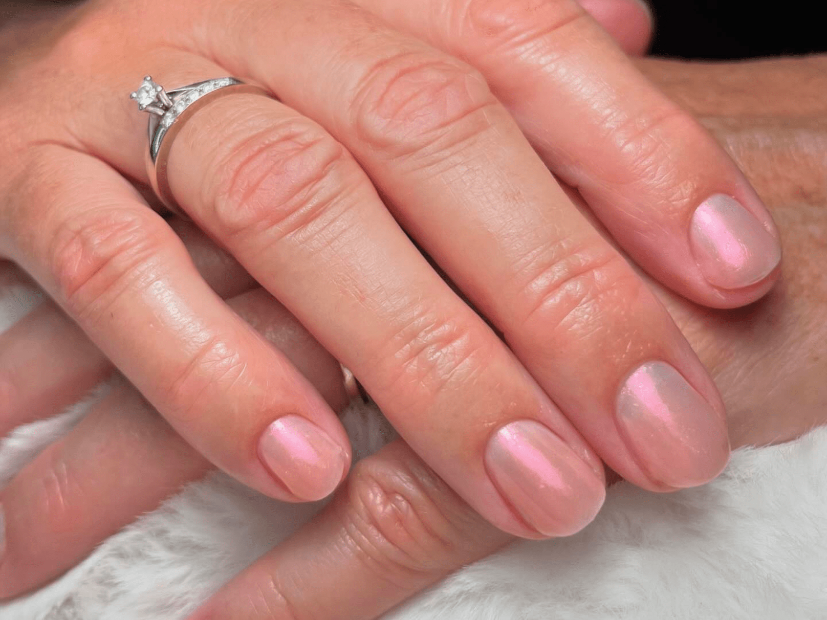 Hand with pink painted nails and a diamond ring.