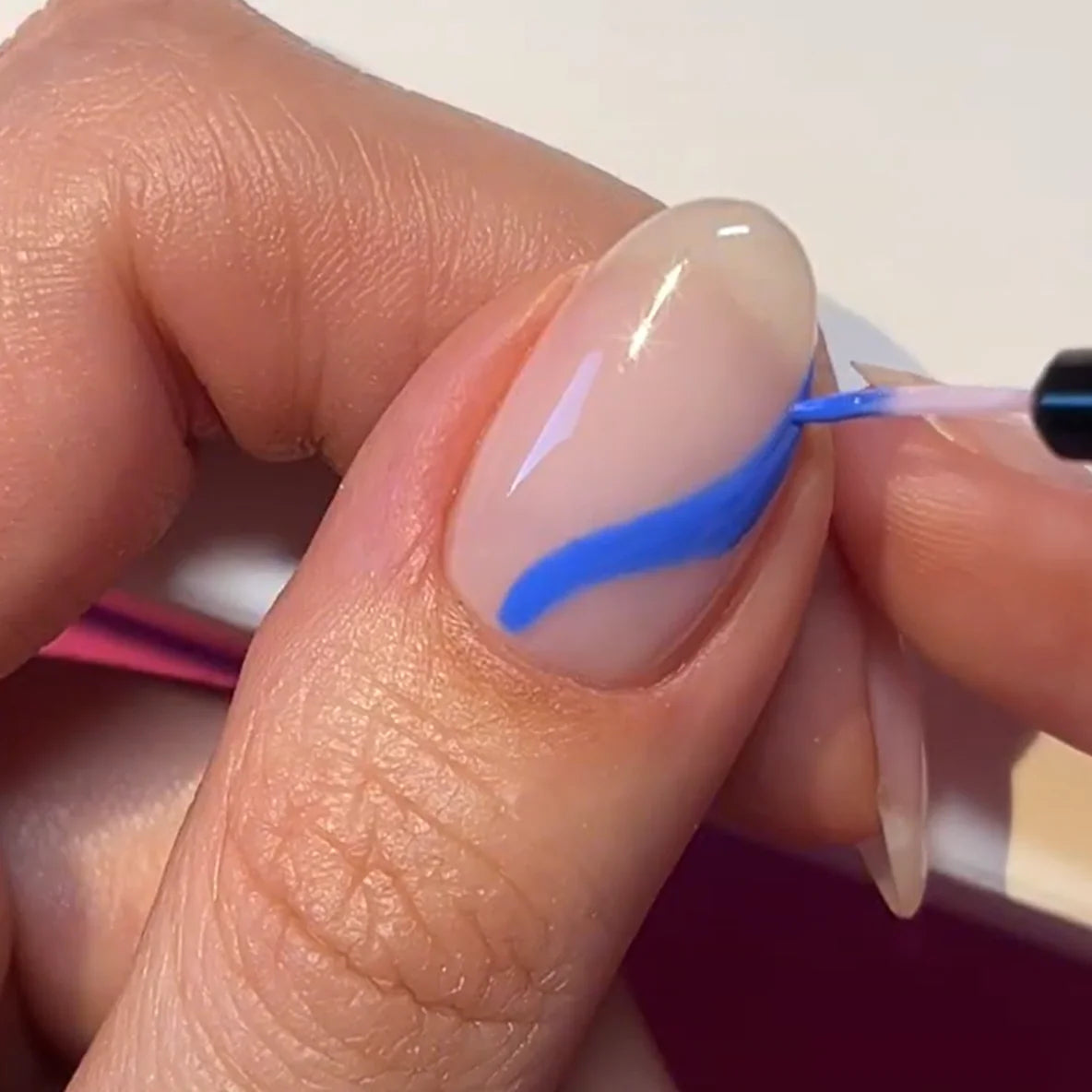 Close-up of a hand with a blue curved line applied to an almond-shaped nail.