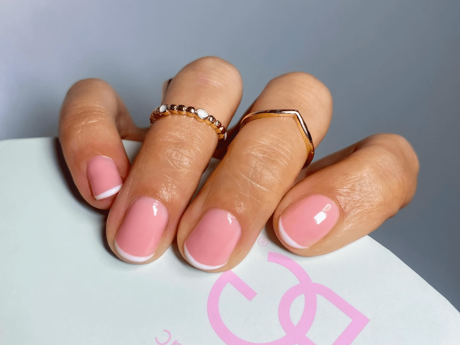 Hand with pink nails and white edges, decorated with gold rings.