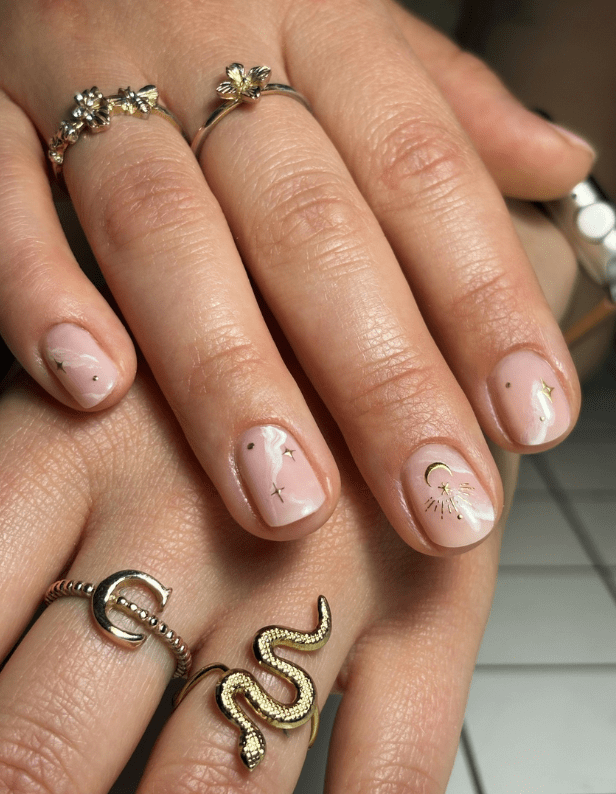 Close-up of a hand with natural nails decorated with subtle star and moon drawings, and worn rings in the shape of flowers, a moon and a snake.