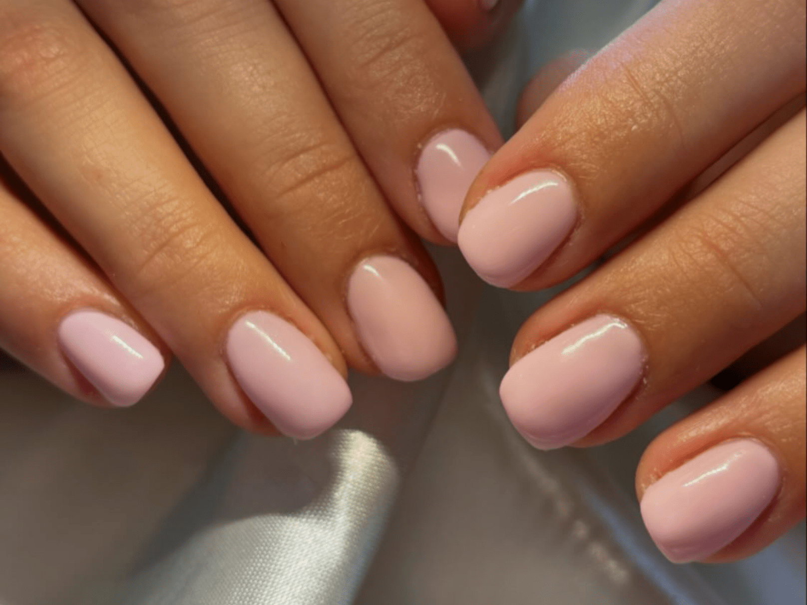 Pink painted nails on hands with a satin background.