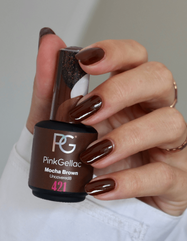 Close-up of a hand with brown painted nails, holding a bottle of Pink Gellac Mocha Brown nail polish.