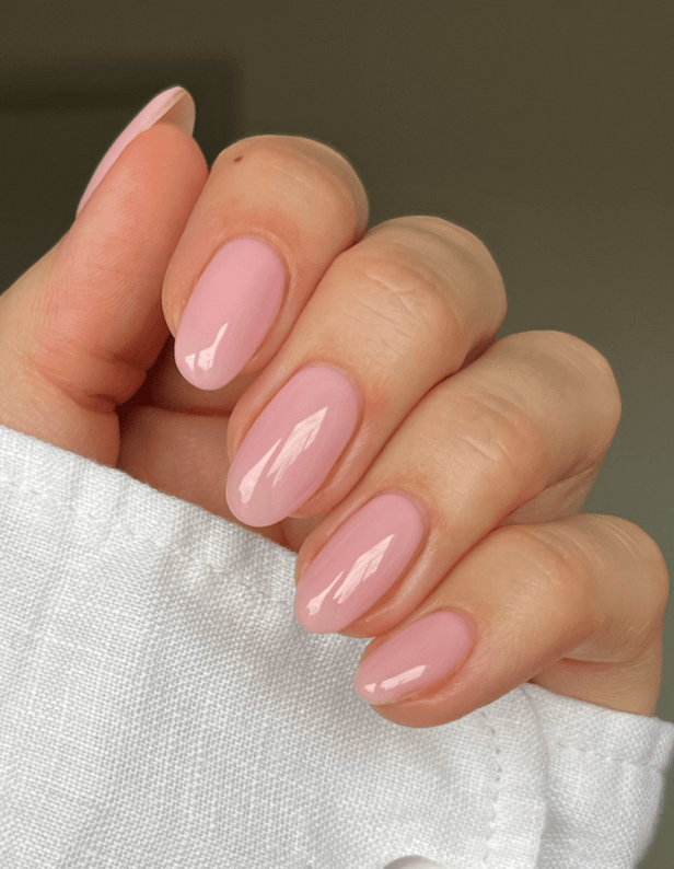 A hand with long, almond-shaped nails with a shiny light pink nail polish.