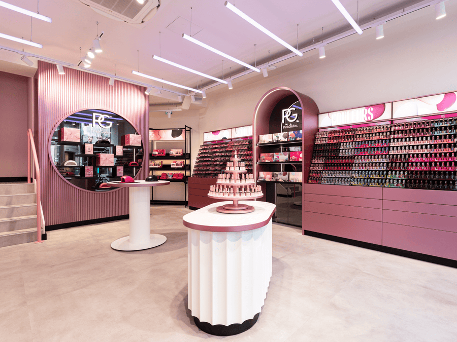 A modern store interior with pink tones, clean lines and stacked displays with nail polish and other beauty products.