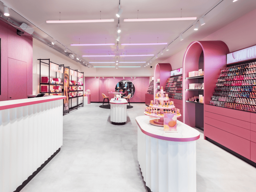 Modern pink store interior with displays full of nail polish and beauty products.
