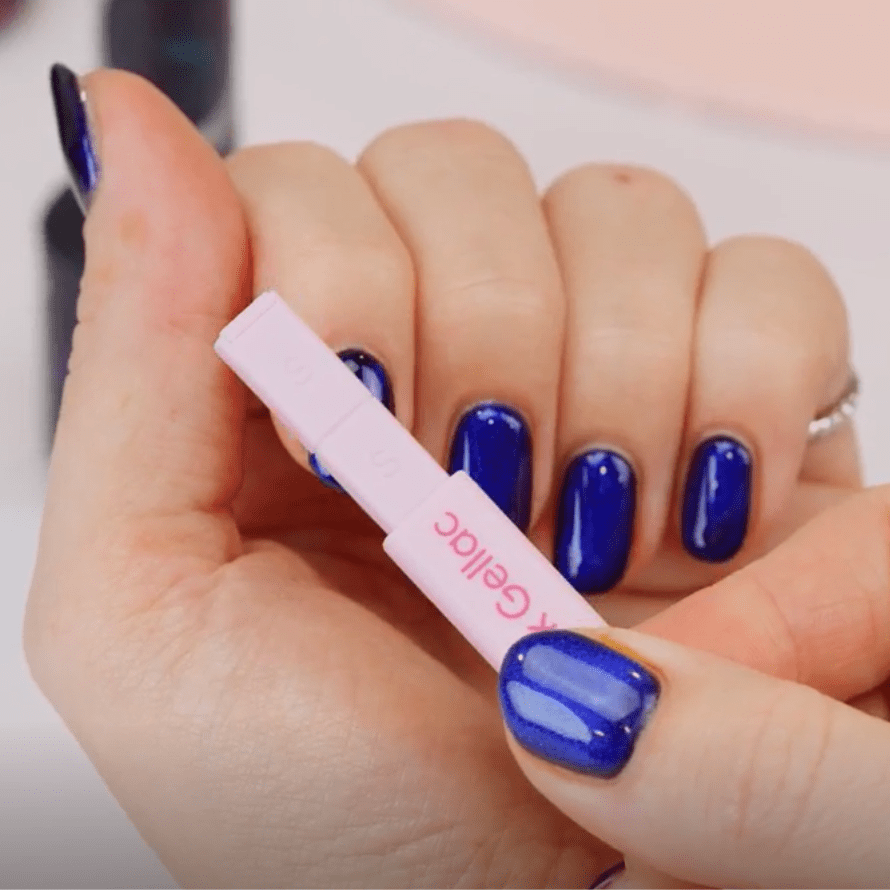 Close-up of a hand holding blue nail polish holding a pink cuticle remover.