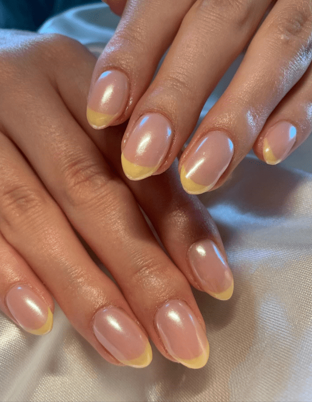 Two hands with graceful nails in a pink pearlescent shade and yellow French manicure.