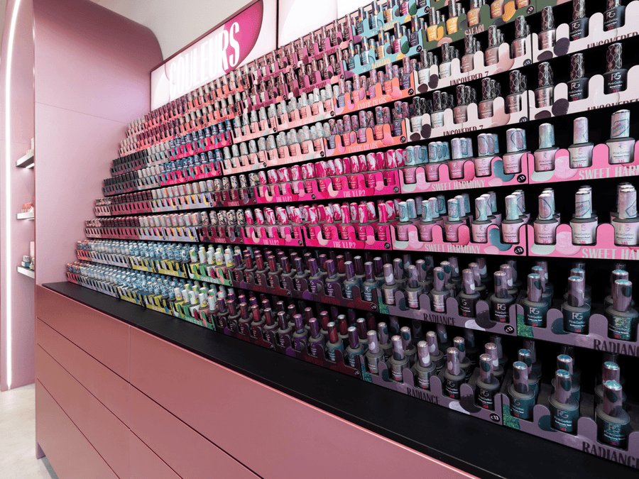 A shop corner with a pink wall on which a large number of colorful nail polish bottles are displayed in different layers.