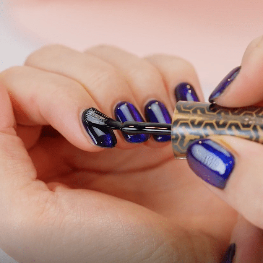A person applies nail polish to nails that are already painted deep blue.