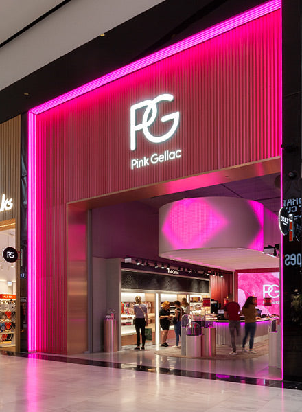 Shop with a striking pink neon entrance, upstairs with the "PG" logo and the name "Pink Gellac"; people are present inside.