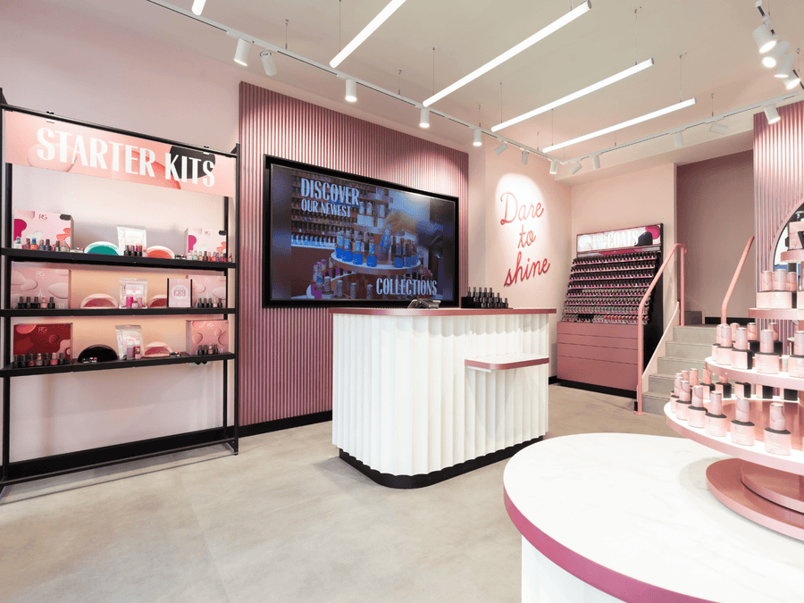 A modern and stylish store layout with a pink color scheme, displays with starter kits, and products on shelves and tables, with a large screen and the text "Dare to shine" in the background.