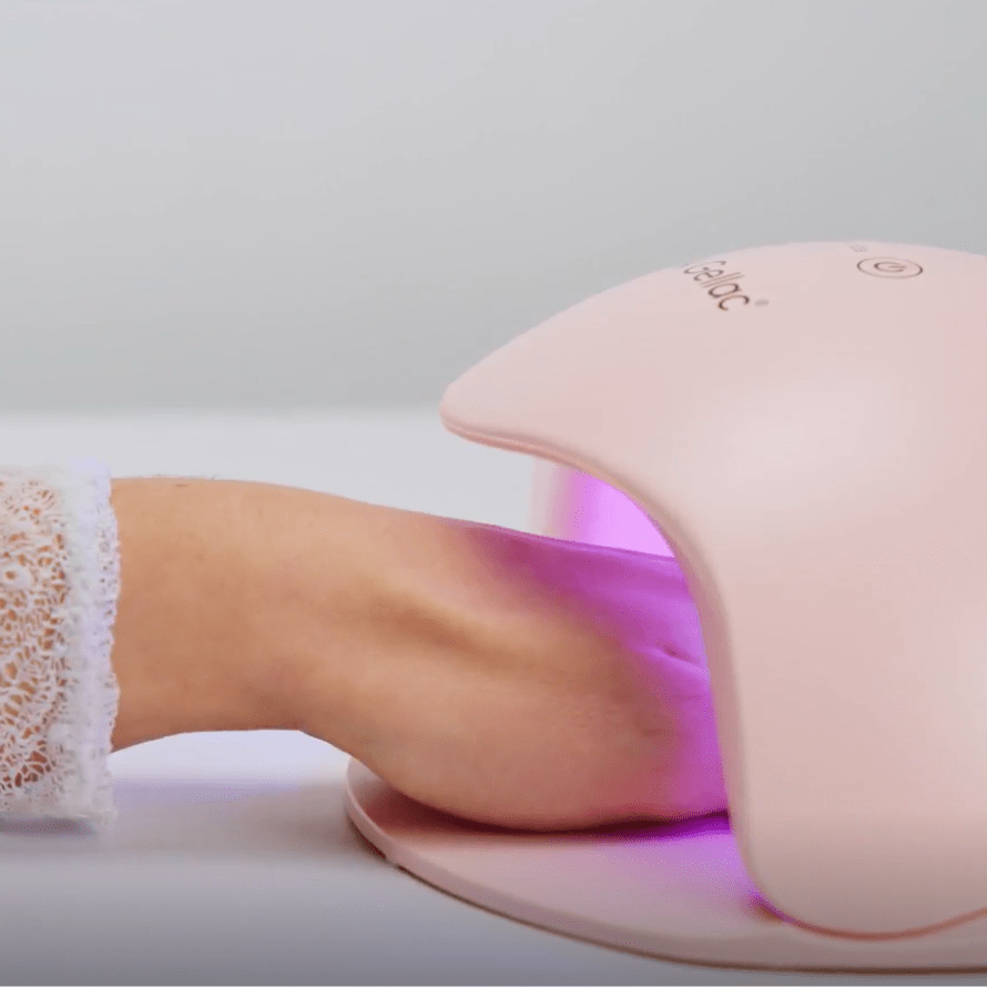 A hand under a pink LED nail dryer with purple light radiation.