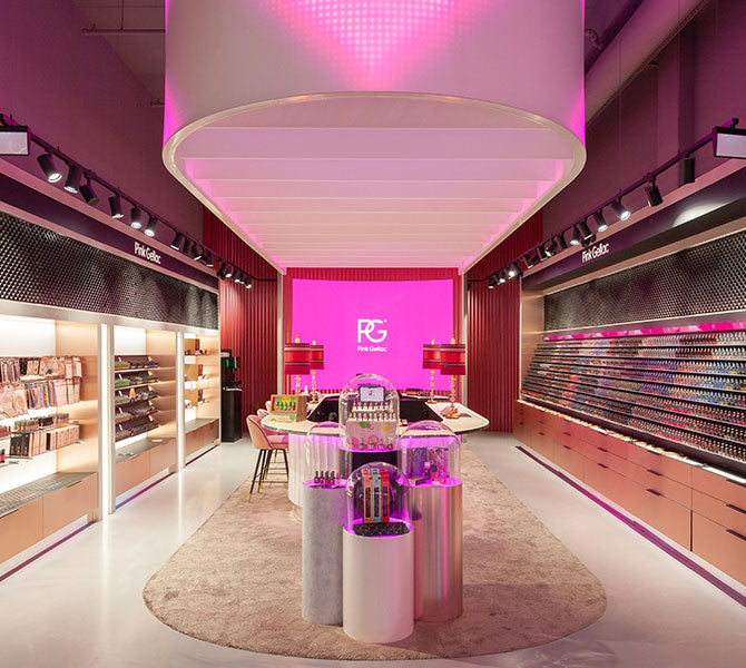 A modern store with a pink and white interior, filled with various make-up displays and illuminated by atmospheric lighting.