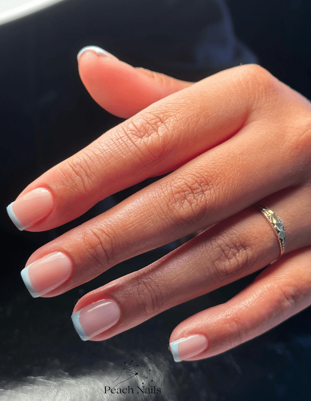 A hand with a gold-colored ring and neatly groomed nails with a light blue French manicure.