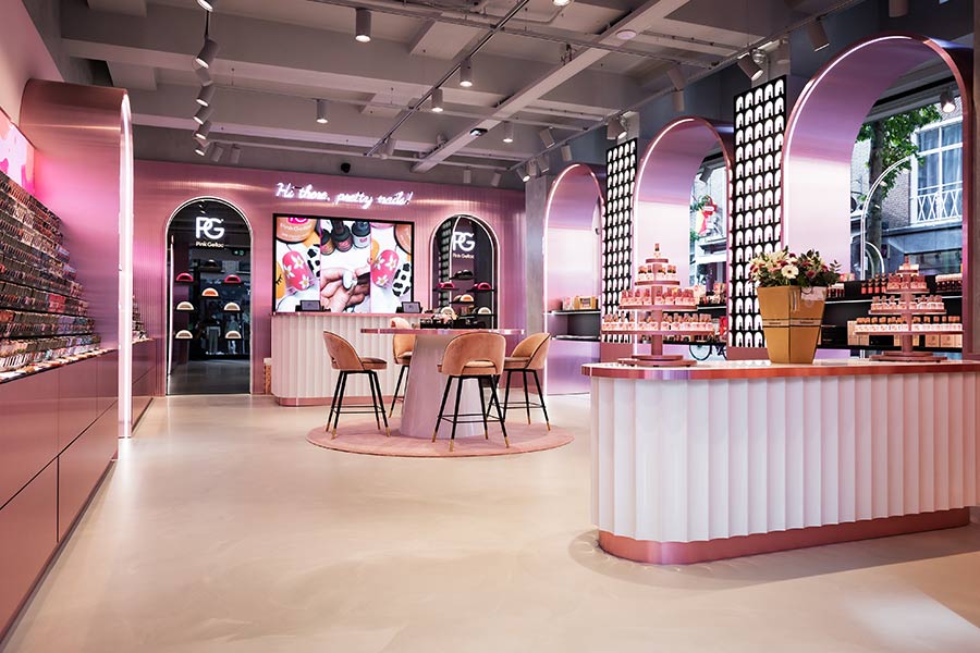 Modern pink makeup shop with displays, high stools, flowers, and large screens. Elegant and stylish décor.