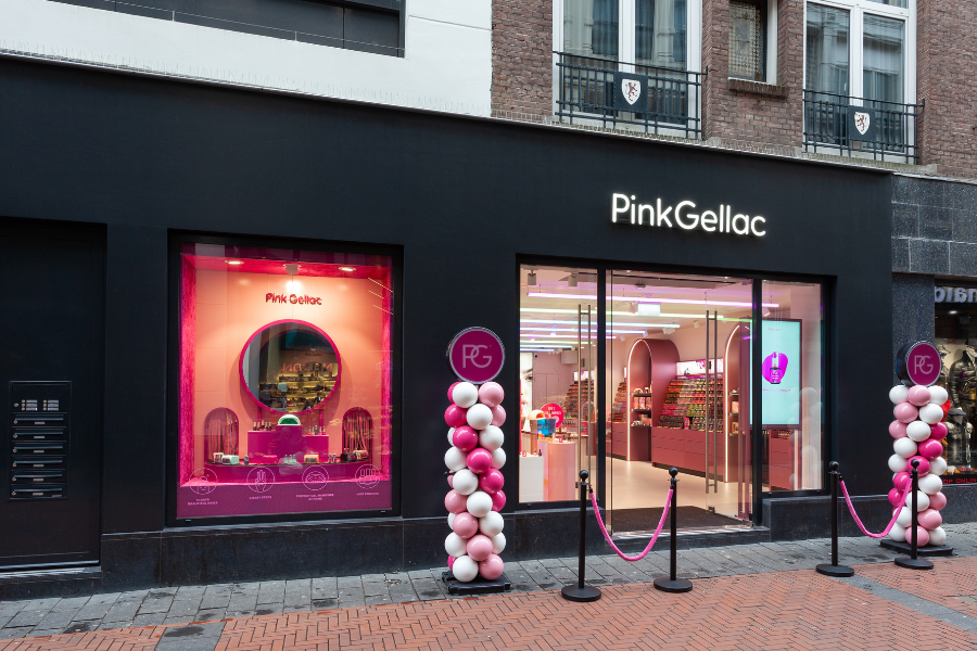 Exterior of a Pink Gellac store with pink and white balloon decorations at the entrance, and a large window overlooking the illuminated and colorful interior.