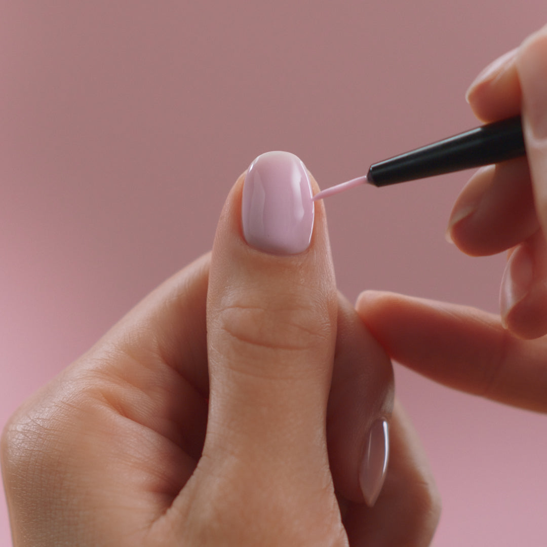 A hand is varnished with light pink nail polish on a pink background.