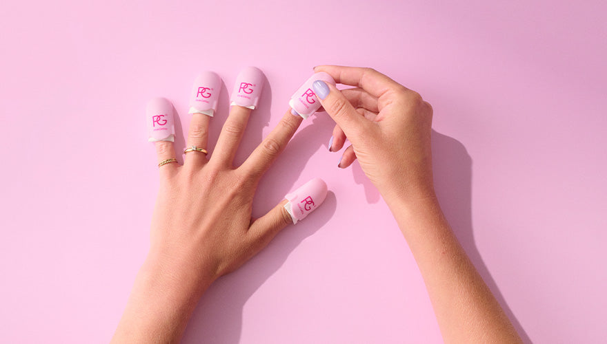 Two hands against a pink background, one©©of which is in the process of placing pink fingertip protectors with white straps and a pink logo on the fingers of the other hand.