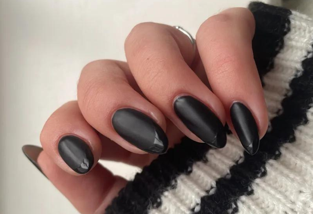 Hand with black, matte painted nails and a knitted sweater.