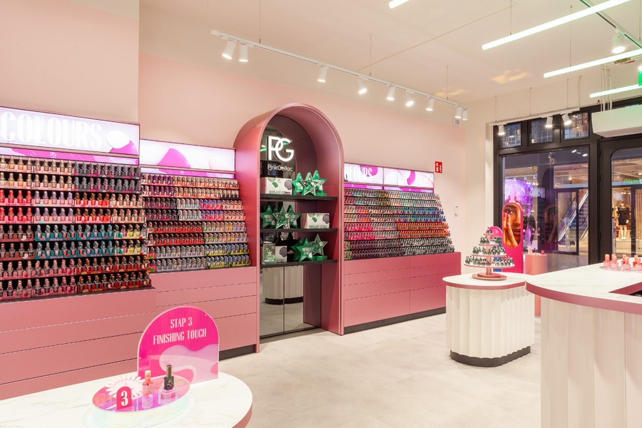 A shop interior with pink walls and displays filled with colorful nail polish bottles, a round table with more products, and a large passageway with green and white packaging.