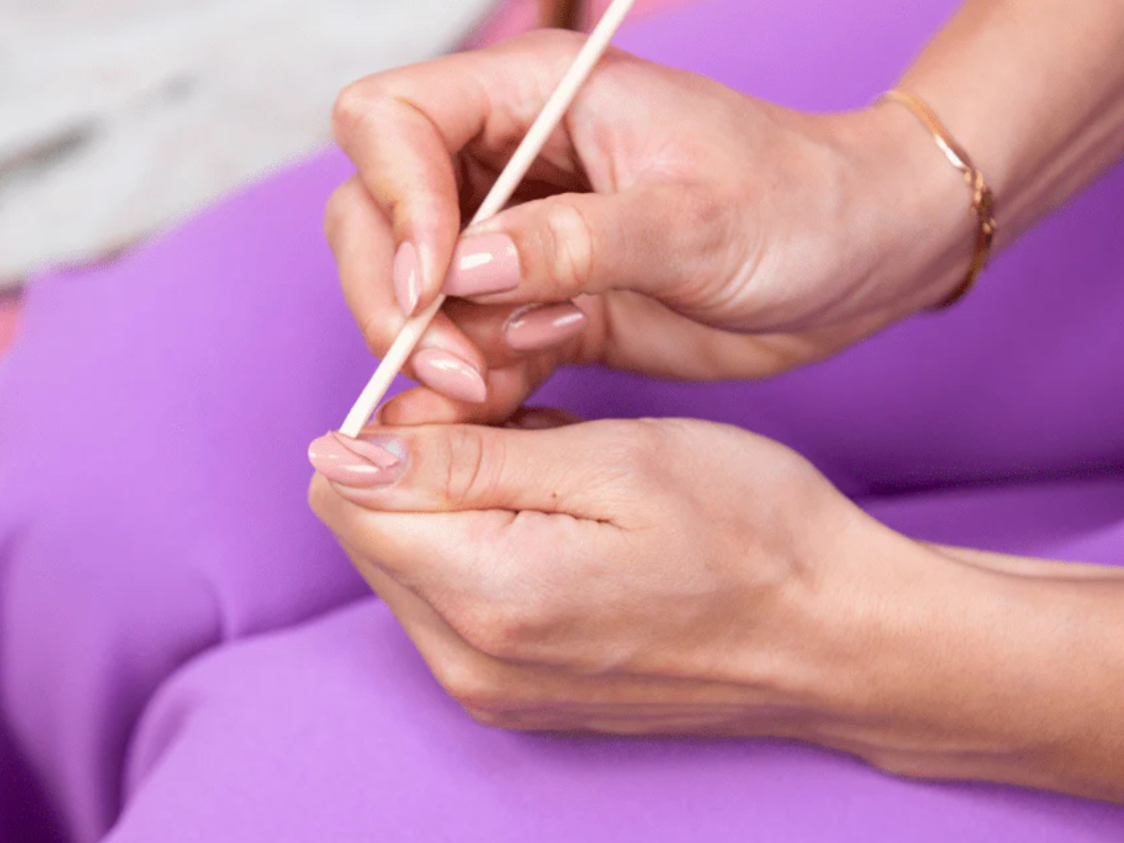 Female hands grooming nails with a wooden stick, sitting on purple fabric.