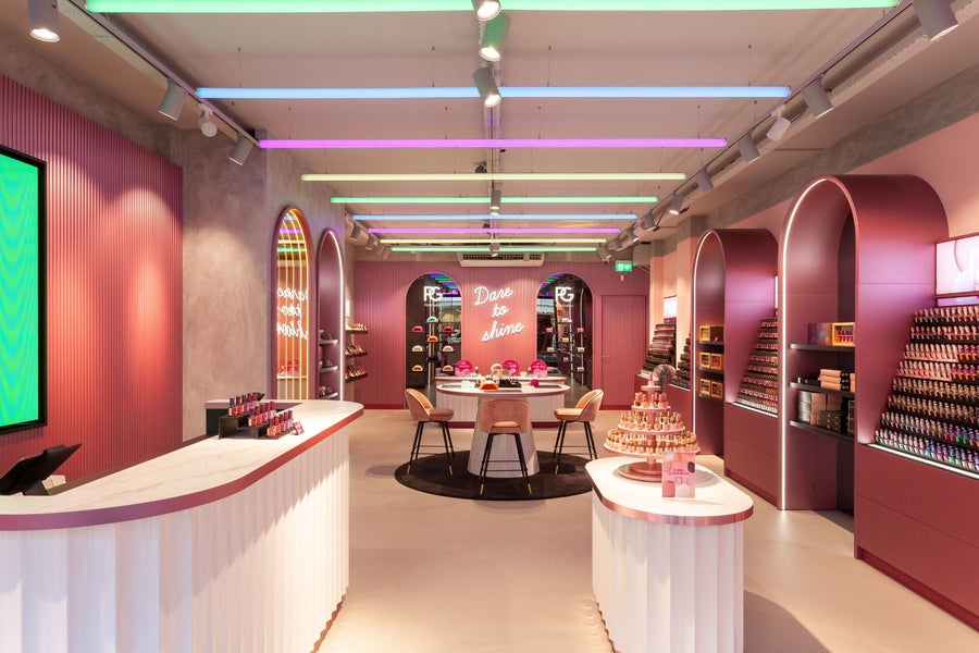Interior of a modern store with colorful lighting, pink and purple walls, a central table with chairs and shelves full of products.