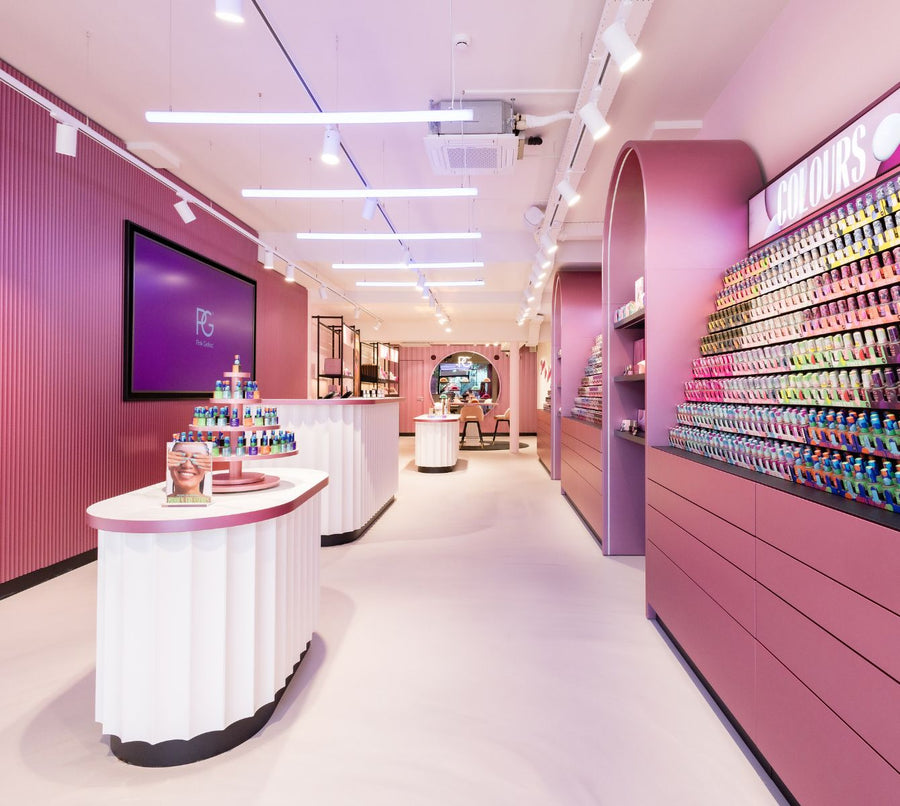 A modern and colorful retail space with pink walls, various displays of cosmetics, and a wide range of bottles of nail polish in different colors on a wall.