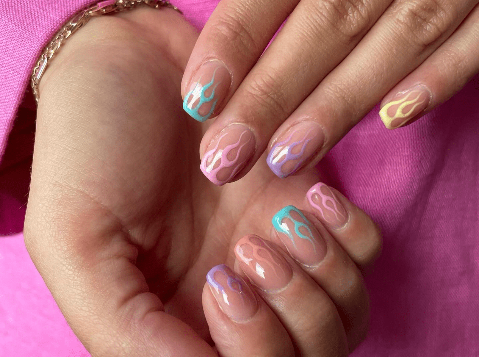 Close-up of hands with colorful nails covered in pastel shades and flame designs.