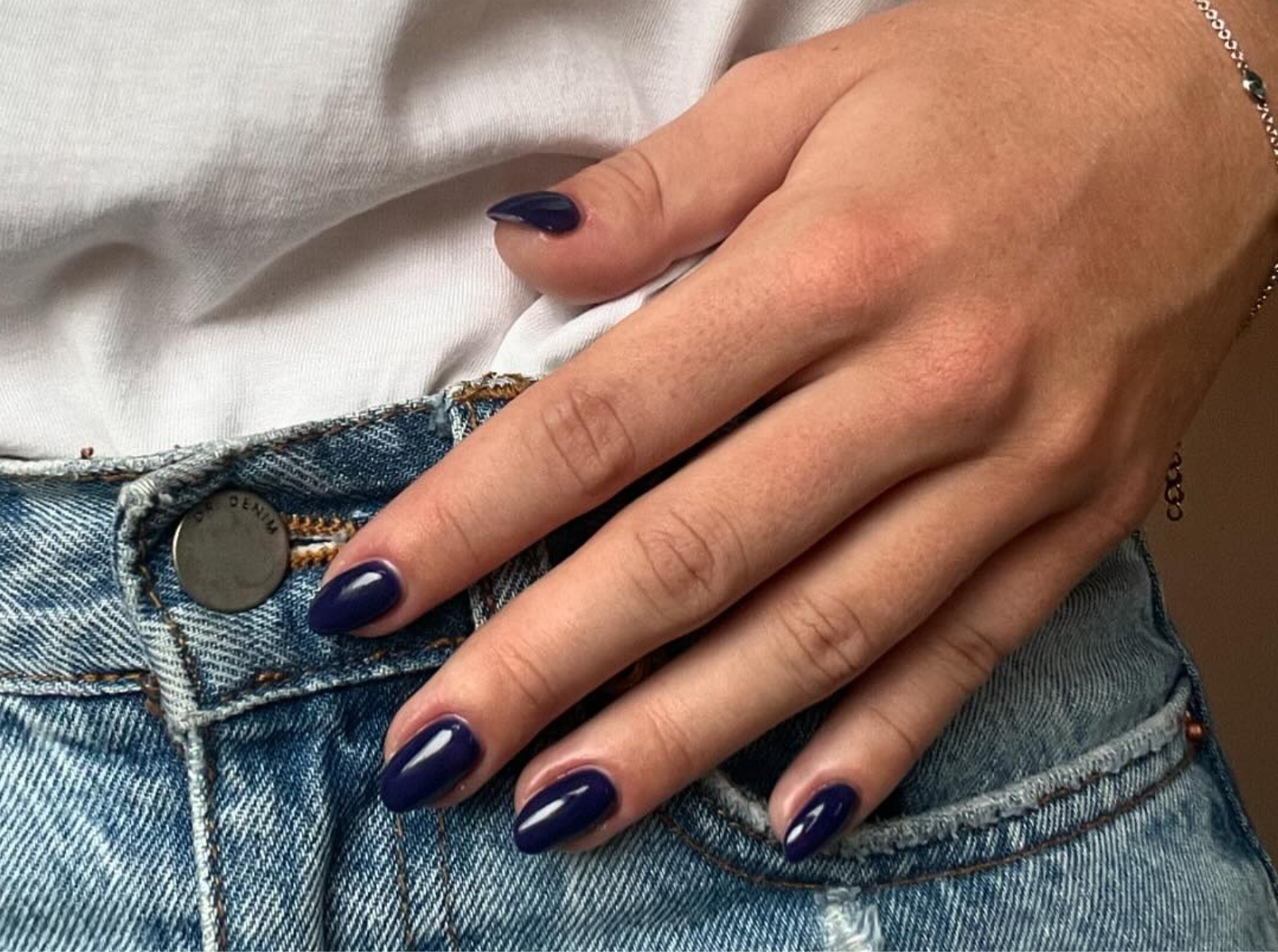 A hand with dark blue painted nails rests on a pair of light blue jeans with a white top.