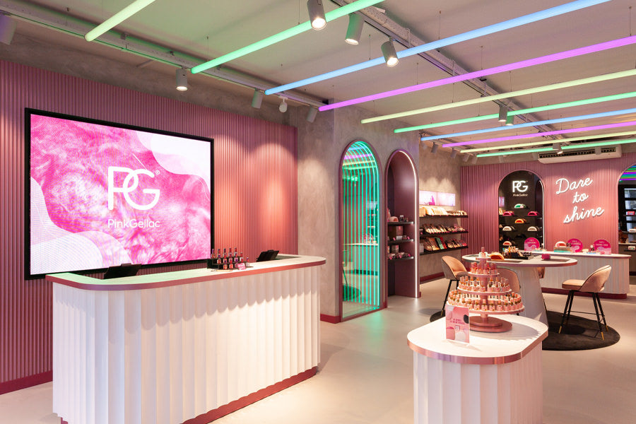 A modern nail polish shop with a pink and colorful interior, illuminated displays and eye-catching LED lighting on the ceiling.