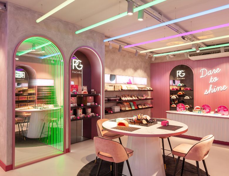 A modern and colorful makeup store with neon lighting, products on shelves, round tables and pink chairs.