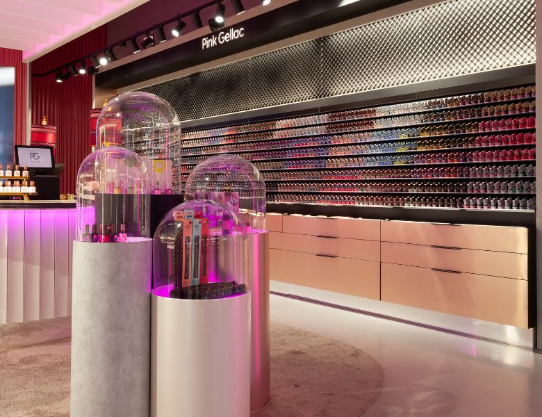 Shop interior with displays of nail polish bottles under glass domes and a wall with various colored nail polish bottles.