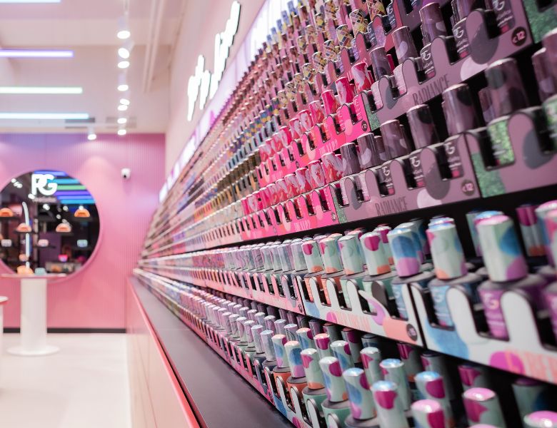 A colorful store with a long wall full of rows of nail polish in different shades and patterns, and a mirror with a logo on the back.