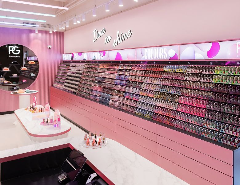 A pink shop interior with racks full of nail polish in different colors, a neon sign with the text "Dare to shine" and a central counter with cosmetics displays.