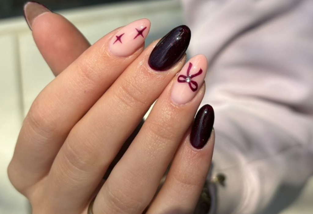 Close-up of a hand with different nail designs; Some nails are painted dark purple and others are decorated with purple stars and bows on a light pink background.