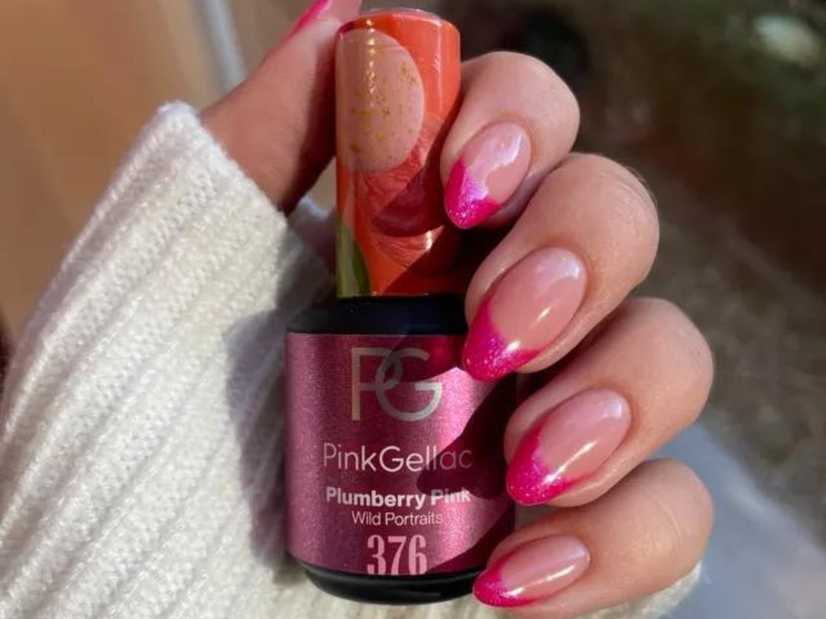 Hand with pink gel nail polish and pink glitter nails, hold a bottle of Pink Gellac in the color Plumberry Pink.