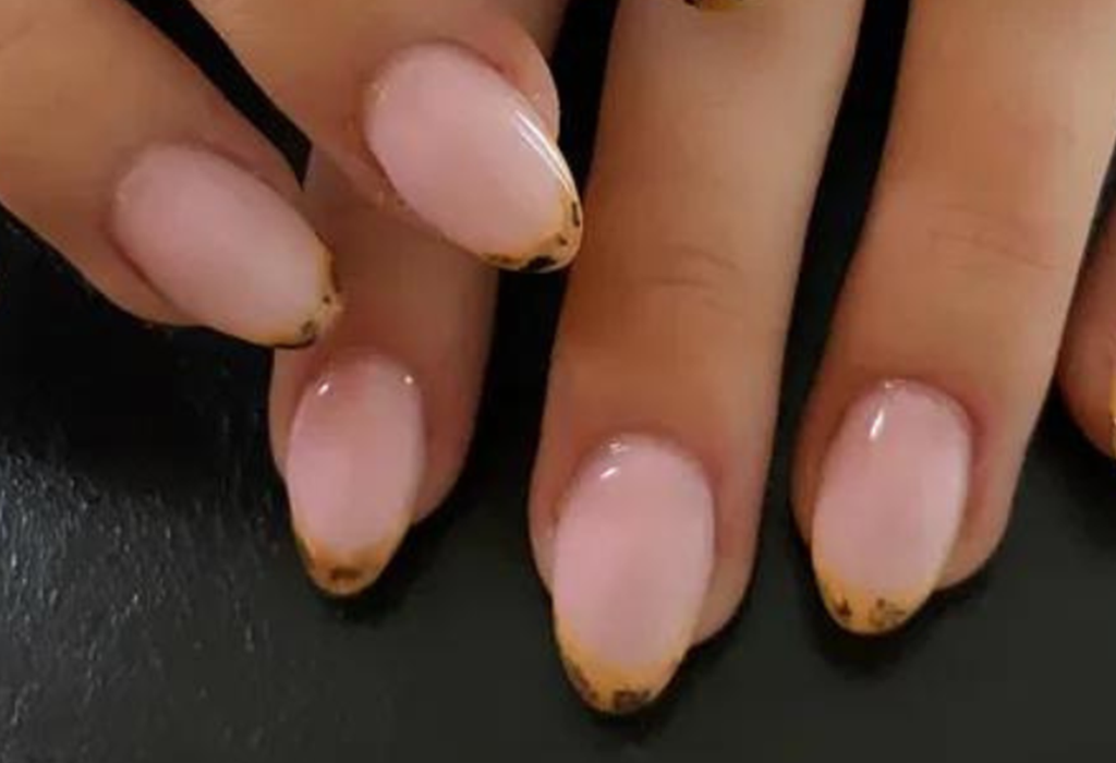 Hand with nails in pink manicure with golden nail tips.