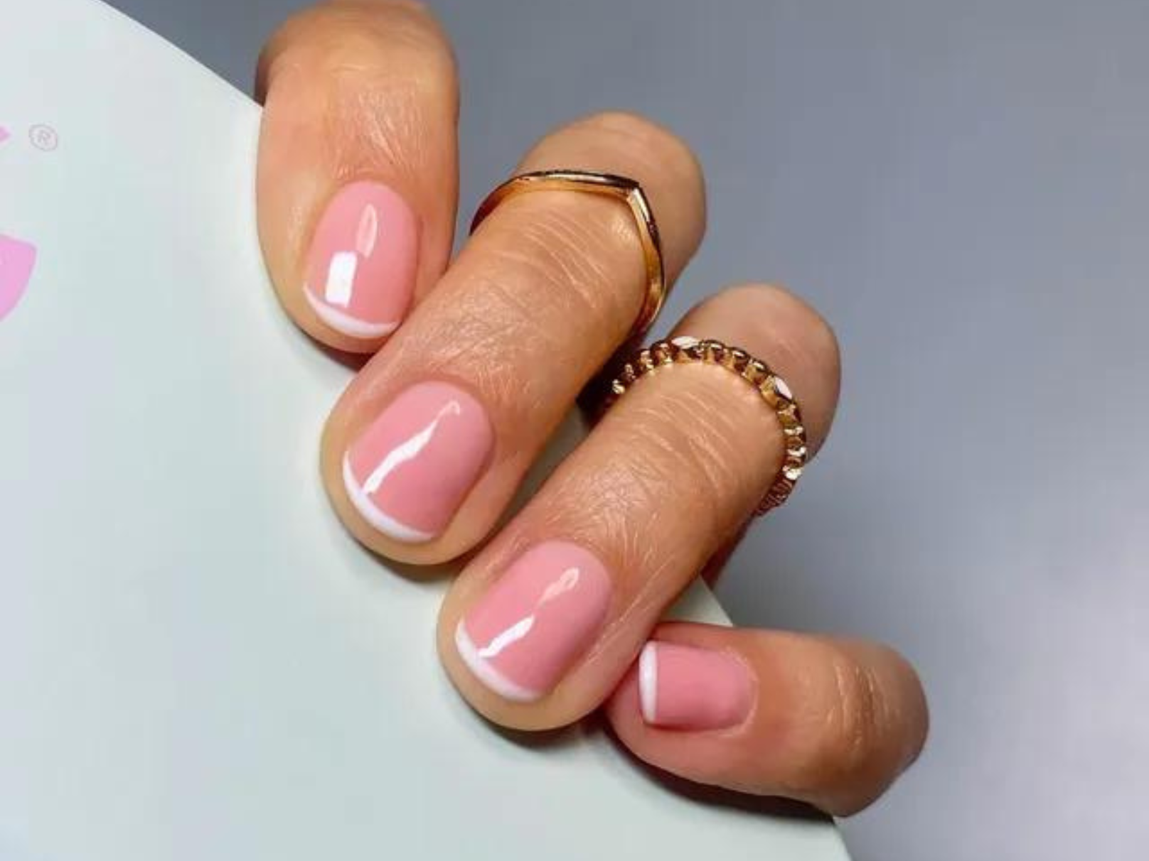 Close-up of a hand holding a French manicure and gold rings.