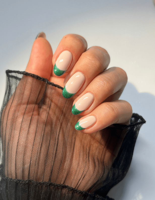 Hand with nails in a French manicure style, with green shimmers at the ends, on a black transparent fabric.
