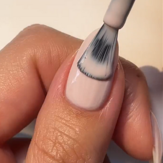 A hand applying a light nail polish to a nail with a brush.
