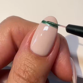 Close-up of a hand painting a subtle, green line on a pale pink painted nail.