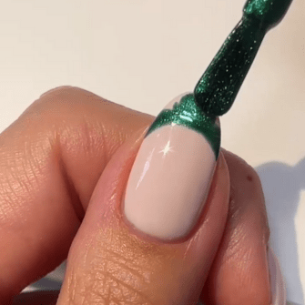 A hand showing a nail with a shiny green nail polish applicator applying green polish to the top edge of the nail.